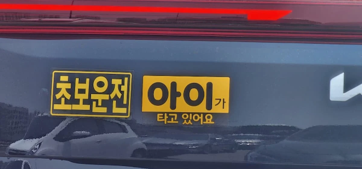 차량 트렁크 상단에 노란색 바탕의 초보운전 표지와 아이가 타고 있어요 표지가 부착된 모습